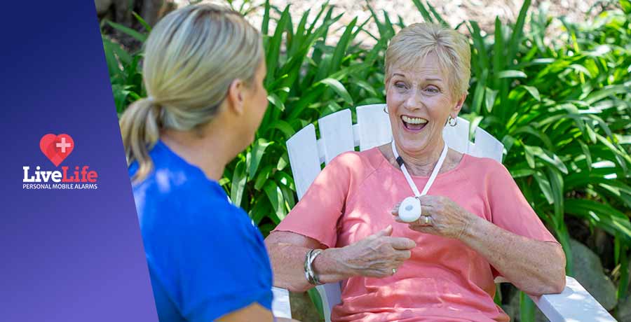 Older lady wearing a white LiveLife Pendant, smiling at carer.