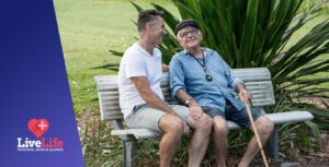Carer supporting senior man who is wearing a Live Life personal alarm in the park